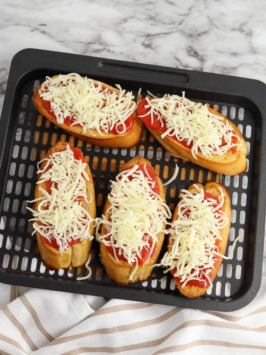 A baking tray with four bread slices topped with tomato sauce and shredded cheese, ready to be baked.