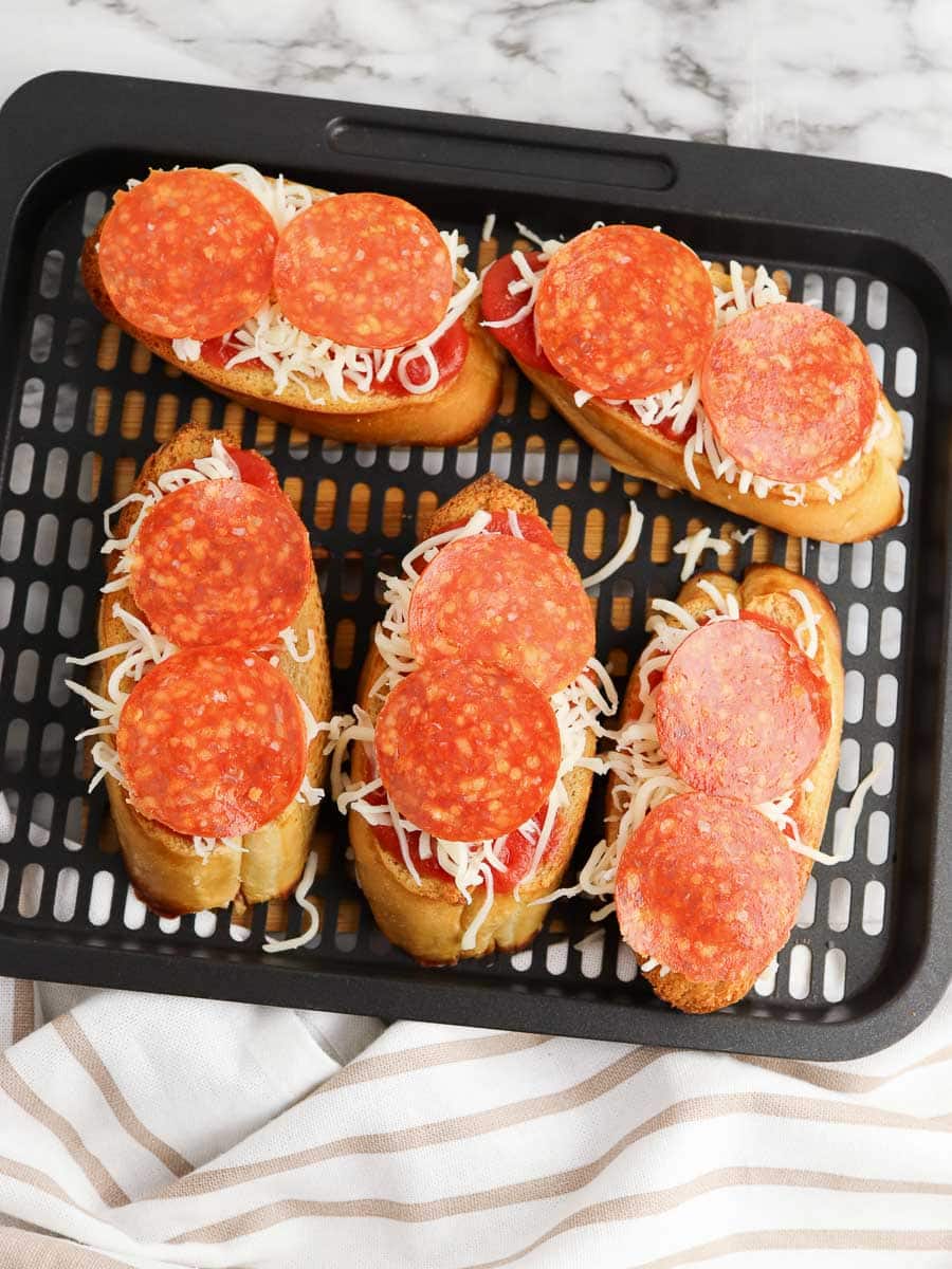 A tray of freshly made pepperoni and cheese mini baguette pizzas on a black tray, set on a marble countertop beside a striped napkin.