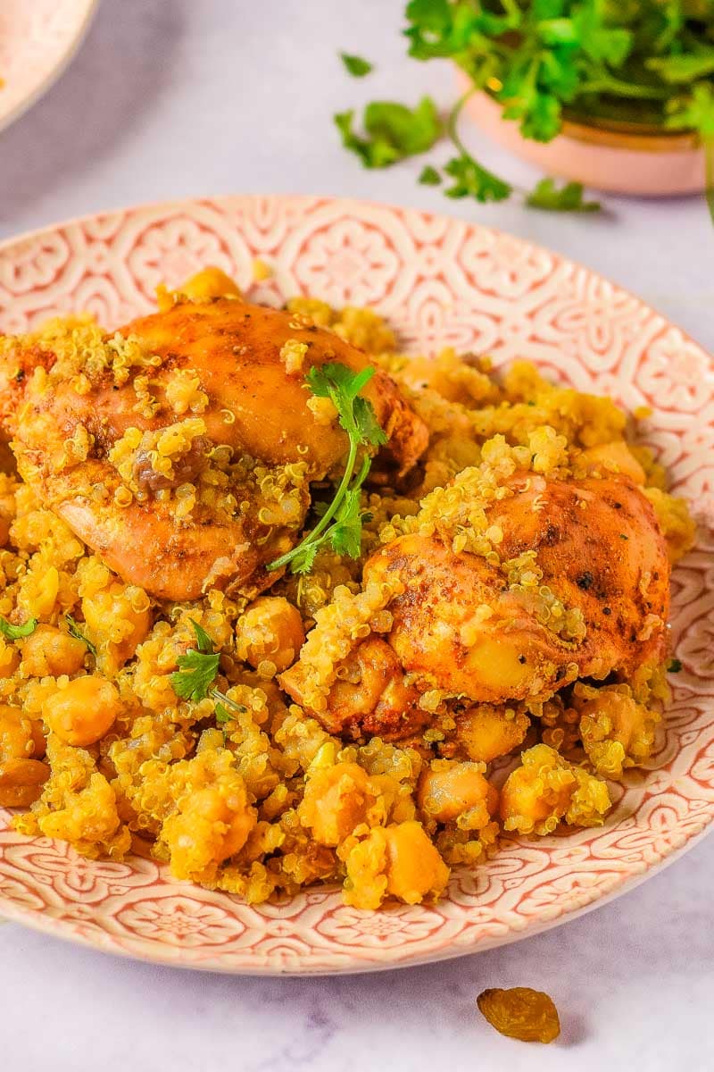 A plate of Moroccan chicken thighs with quinoa and chickpeas, garnished with fresh parsley.