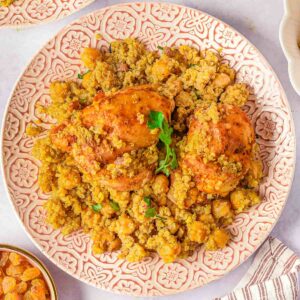 A plate of Moroccan chicken thighs tagine with quinoa and chickpeas, garnished with fresh parsley.