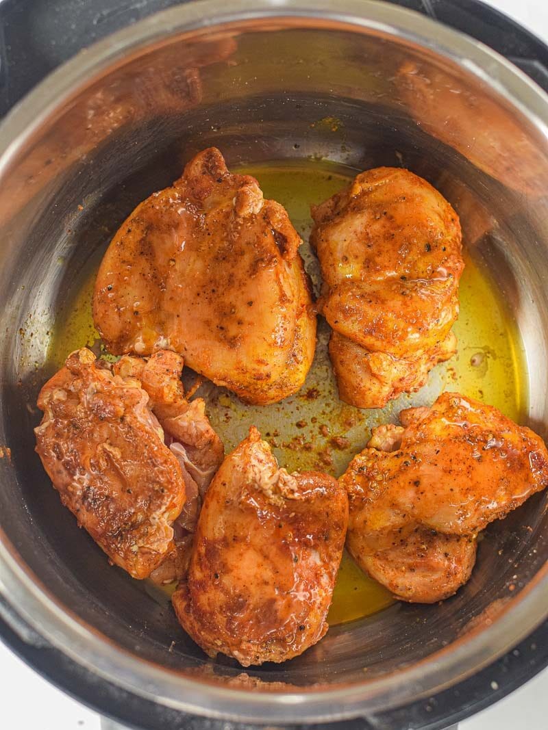 Moroccan seasoned chicken thighs cooking in oil inside an instant pot.