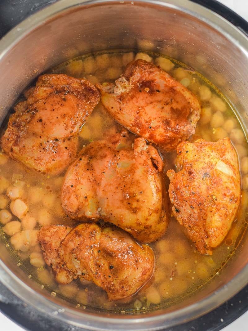 Moroccan spiced chicken thighs cooking with chickpeas in a stainless steel pressure cooker.