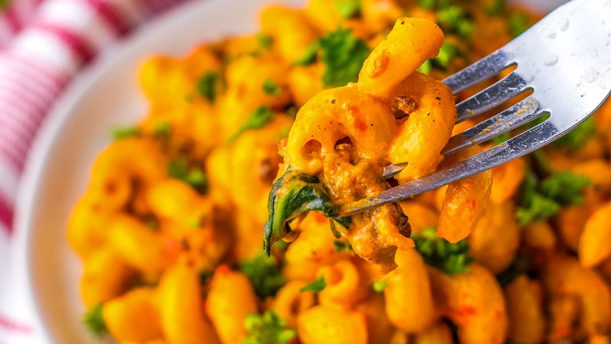 A close-up of a fork lifting a Sausage Pepper Pasta dish garnished with herbs.