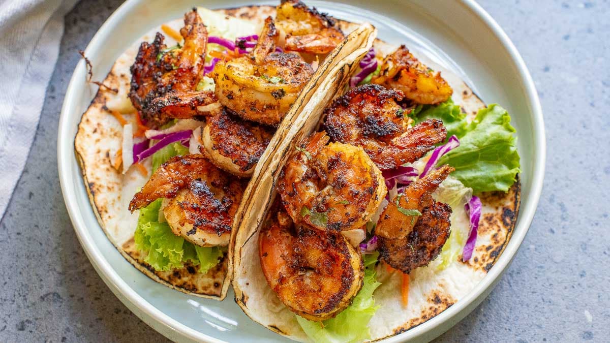 Shrimp tacos with cabbage and lettuce on a white plate.
