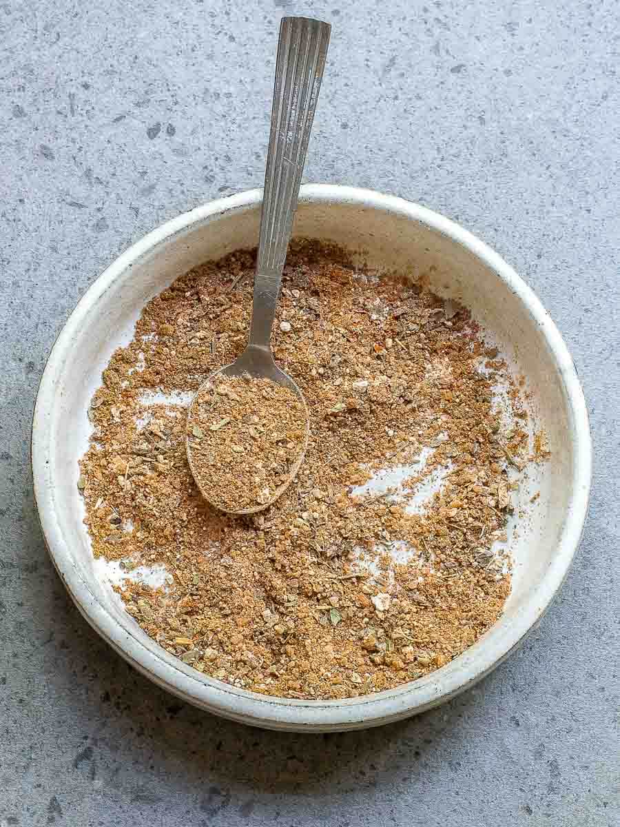A bowl of ground spices with a spoon on a gray surface.