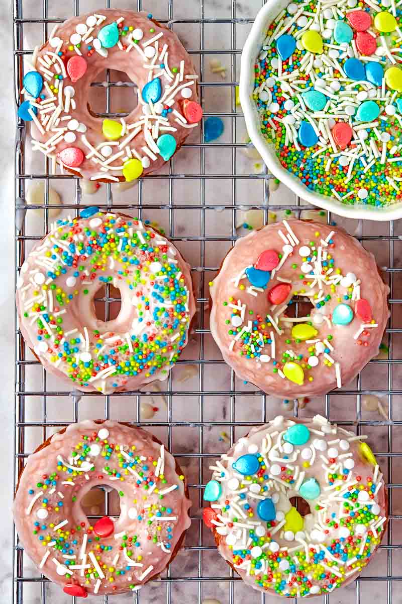 Assorted frosted donuts with colorful sprinkles and candy toppings on a wire rack.