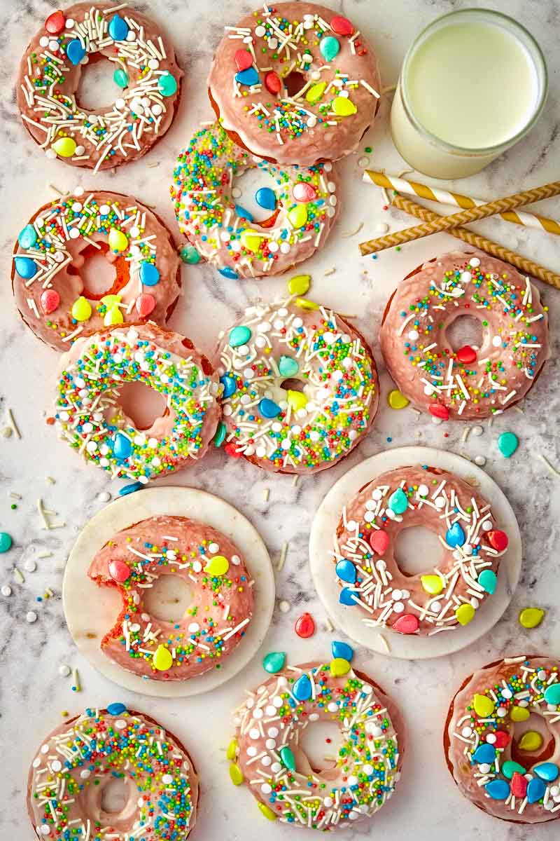 A variety of colorful frosted doughnuts with sprinkles and candy toppings, accompanied by a glass of milk.