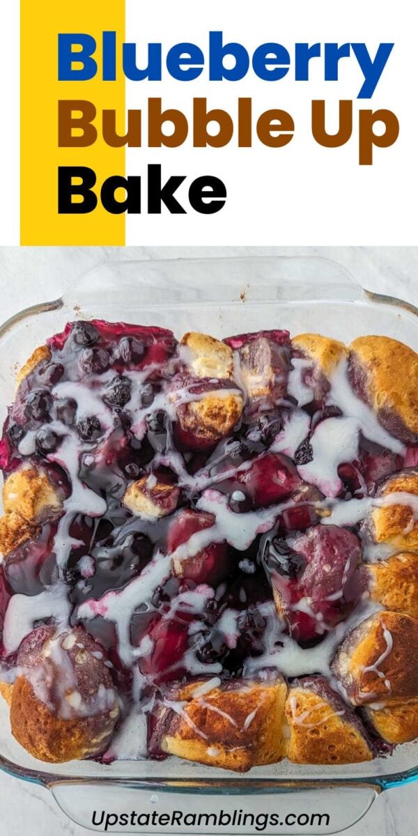 A baked blueberry bubble up dessert in a glass dish, topped with icing and golden-brown biscuit pieces. Text reads “Blueberry Bubble Up Bake.”.