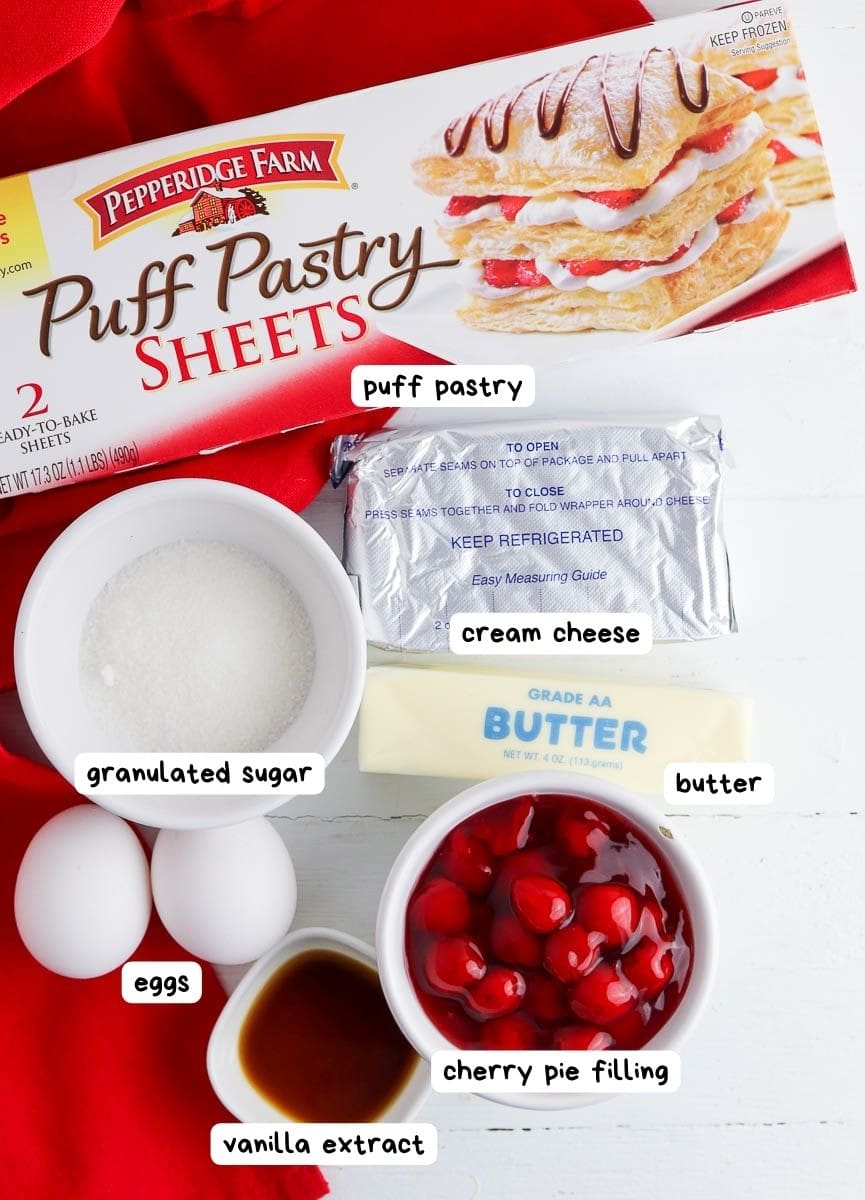 Ingredients for baking displayed: puff pastry sheets, cream cheese, butter, sugar, eggs, cherry pie filling, and vanilla extract, with labeled packaging.