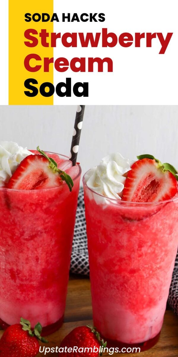 Two glasses of dirty strawberry soda topped with whipped cream and a strawberry, with a striped straw in one glass. Fresh strawberries are placed in front of the glasses.