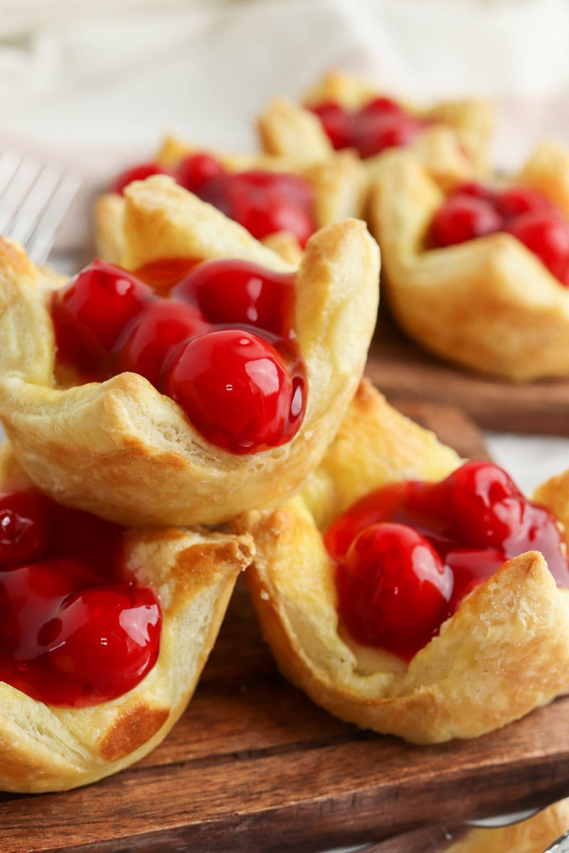 Close-up of cherry pastries on a wooden board, featuring golden-brown, flaky crusts topped with vibrant red cherries.