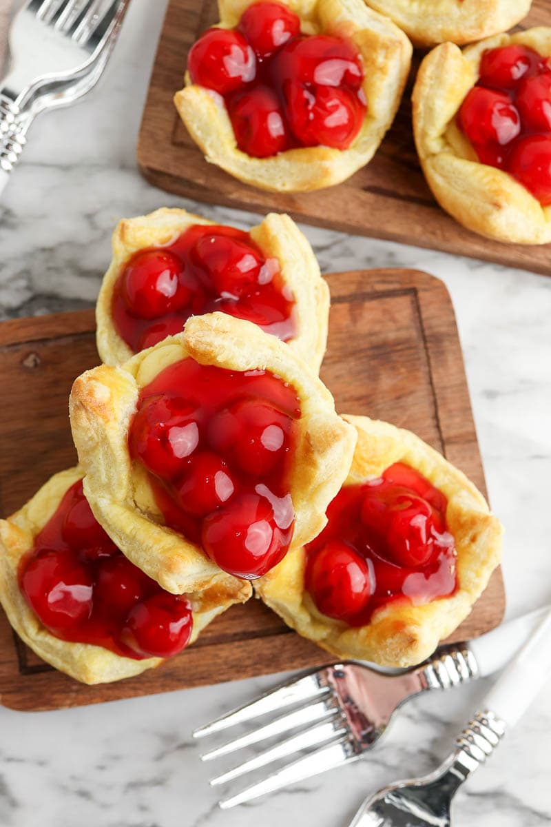 Cherry-filled pastries on a wooden board with forks on a marble surface.