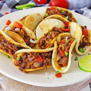 A plate of beef tacos garnished with diced tomatoes and peppers, served with a side of salsa.
