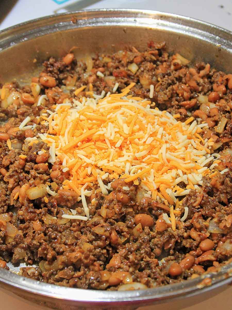 A pan filled with a mixture of cooked ground meat, beans, and corn, topped with shredded cheddar cheese in the center.