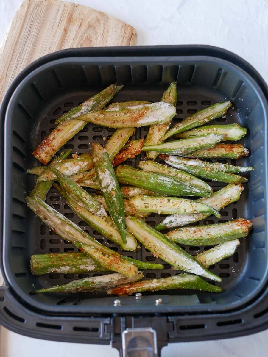 Sliced okra coated in seasoning and breadcrumbs is arranged inside an air fryer basket, ready to be cooked.
