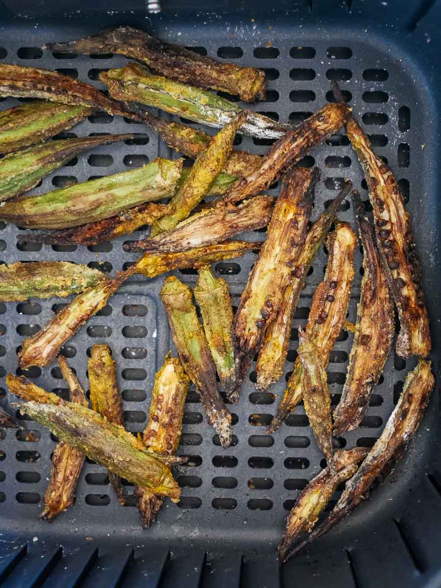 Fried okra pieces in an air fryer basket, some browned and crispy.