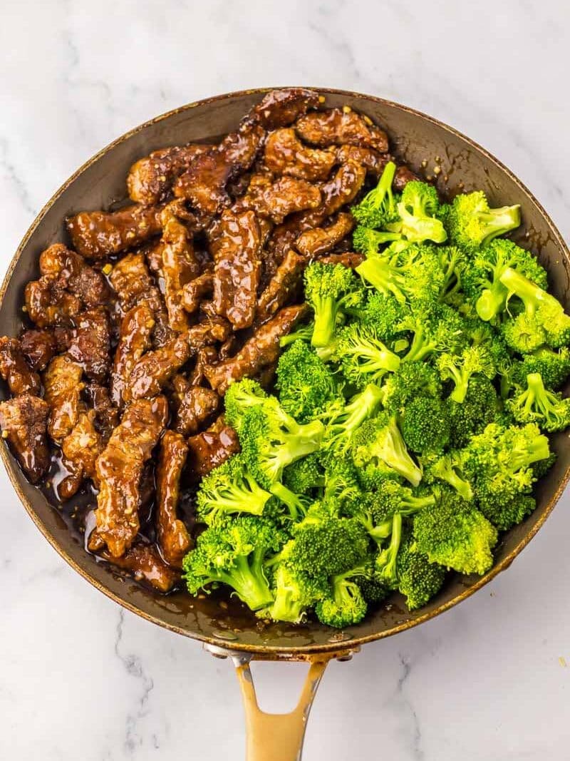A skillet filled with cooked beef strips in a brown sauce on one side and bright green broccoli florets on the other side.