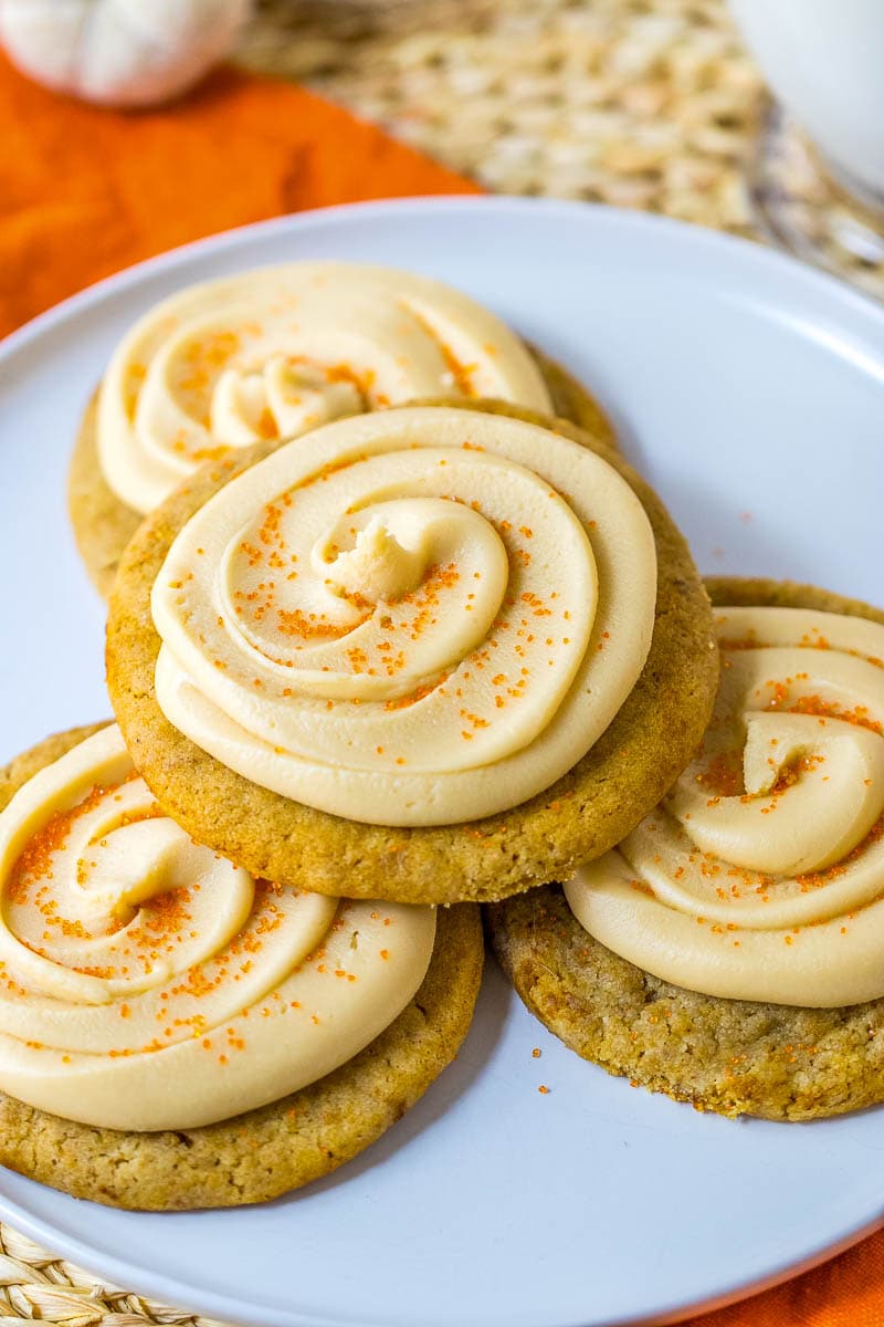 A white plate holds four cookies topped with swirled orange and cream-colored frosting and orange sugar sprinkles.