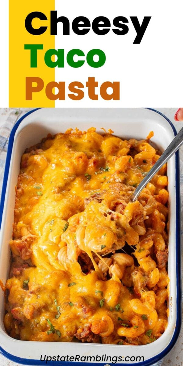 A baking dish filled with cheesy taco pasta casserole topped with melted cheddar cheese, with a serving spoon scooping some out.