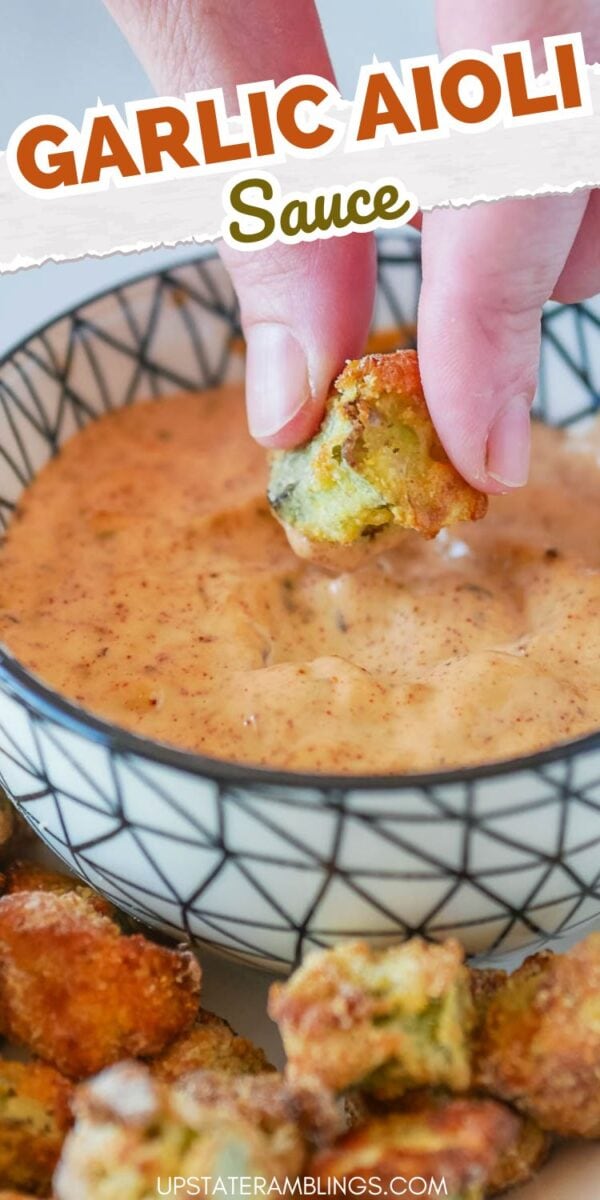 A hand dips a piece of food into a bowl of garlic aioli sauce. The background is filled with similar pieces of food.