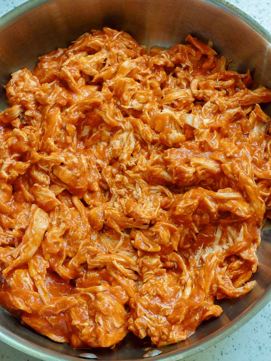 A bowl filled with shredded chicken mixed in a red sauce.