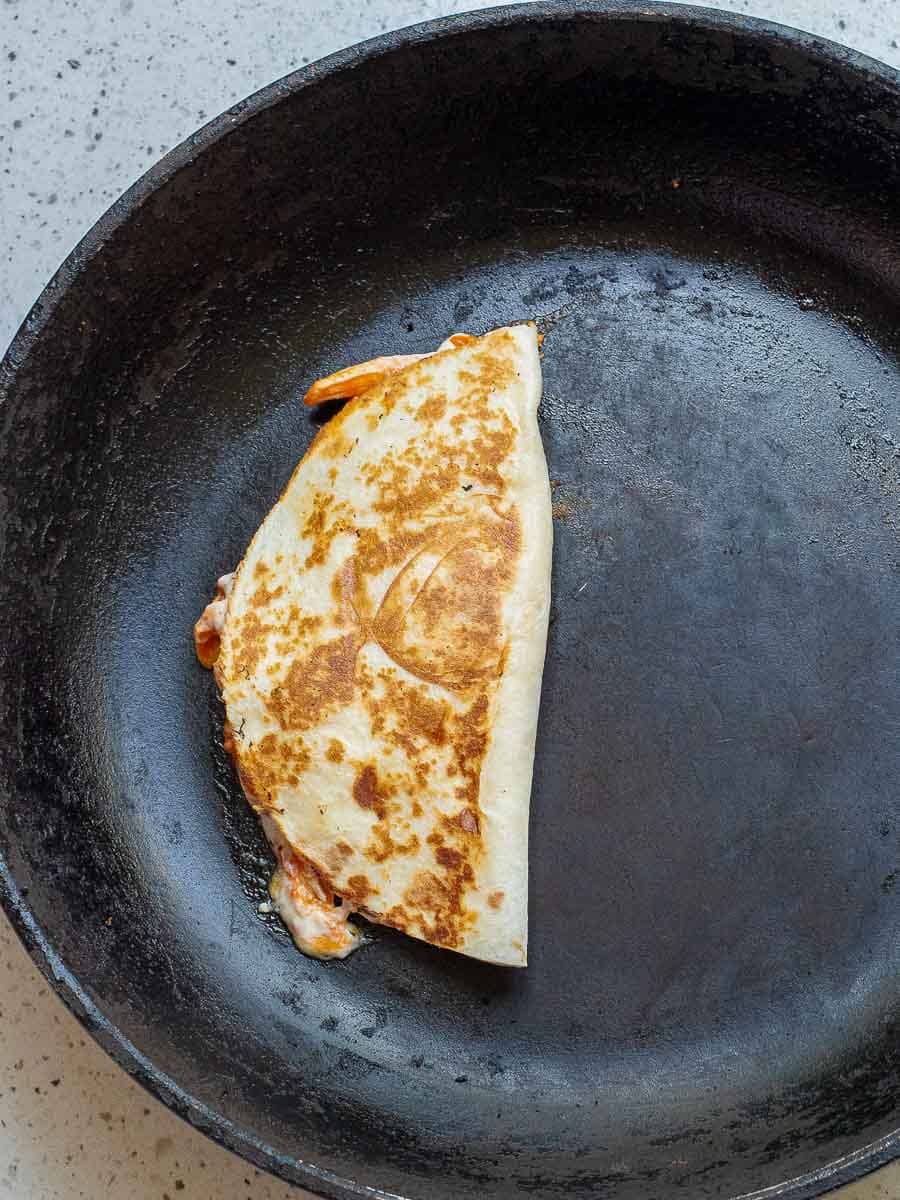 A quesadilla folded in half is being cooked in a black skillet.