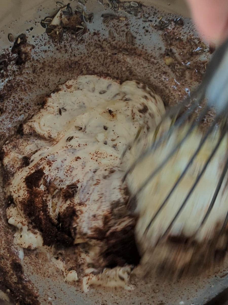 Close-up of ingredients, including cream and what appears to be cocoa powder, being whisked together in a mixing bowl.