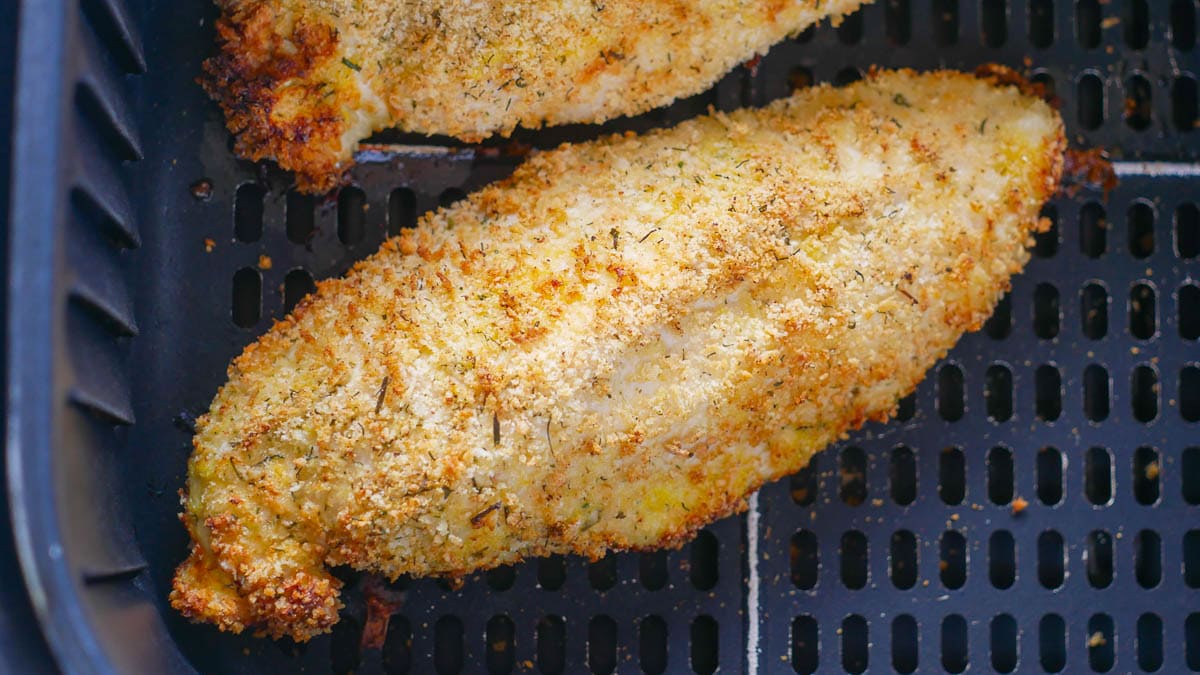 Breaded chicken fillets cooking in an air fryer basket.
