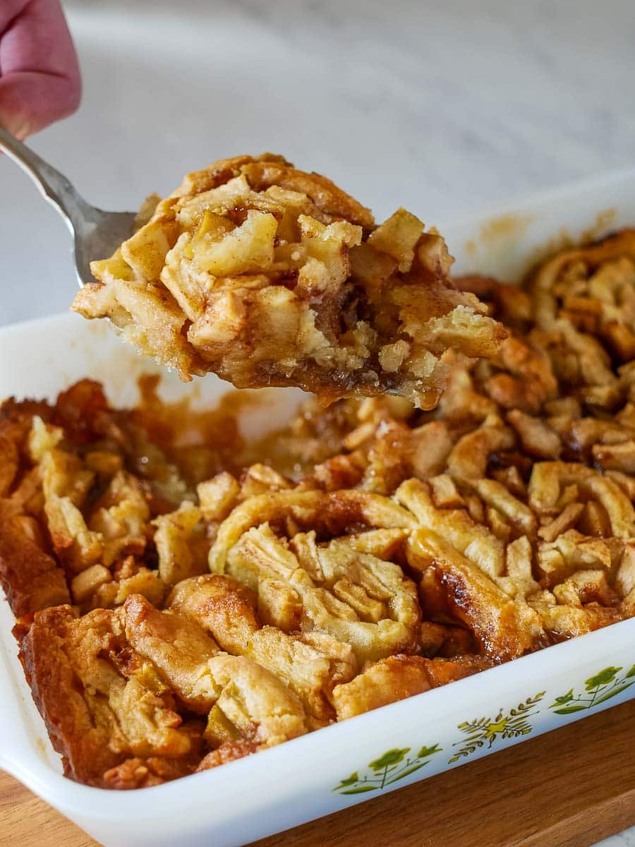 A serving of apple cobbler being lifted from a baking dish with a spoon.