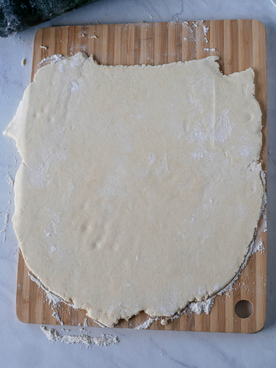A rolled-out sheet of dough on a wooden cutting board, ready for further preparation.