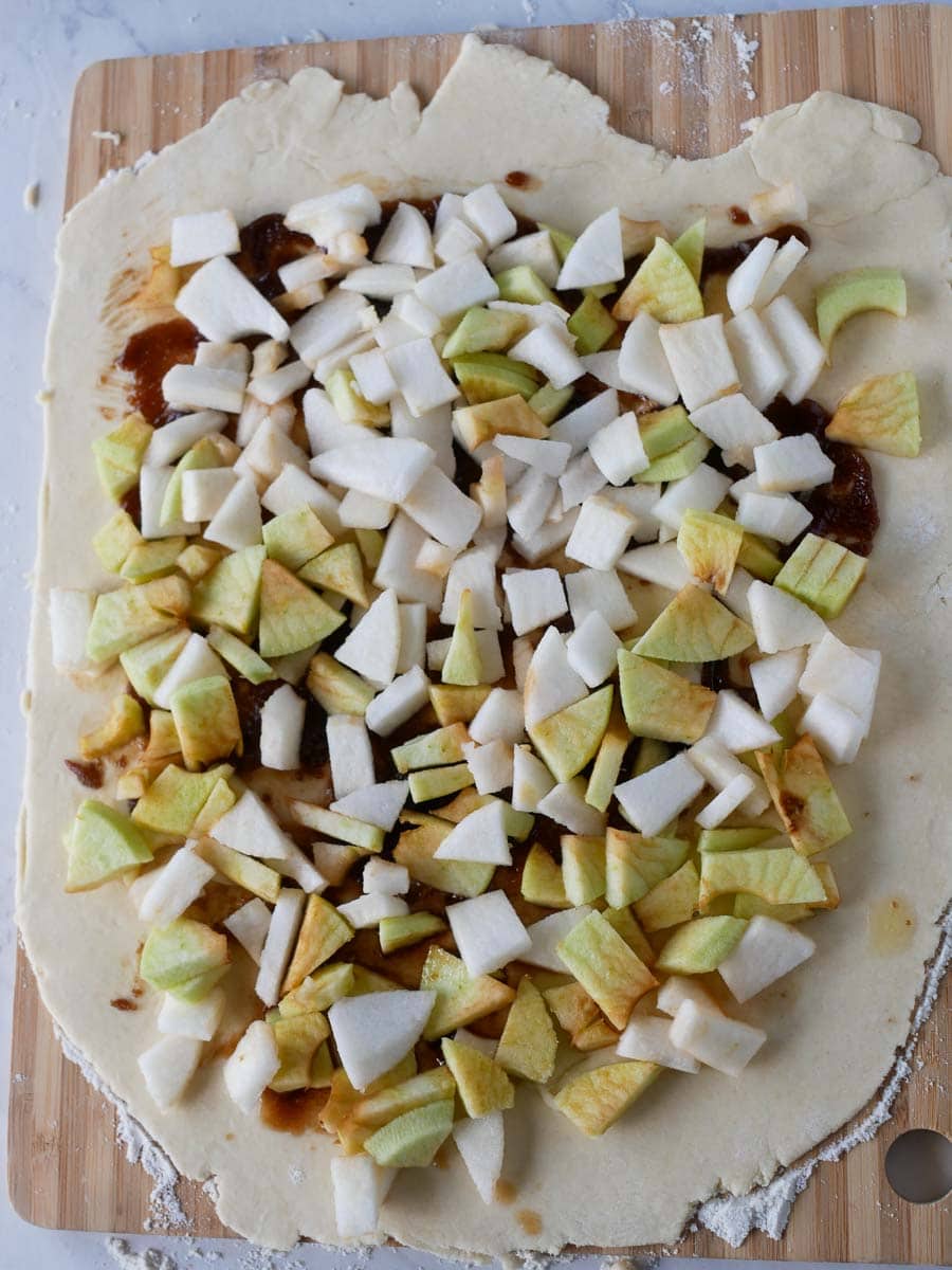 Chopped apples spread over rolled-out dough on a wooden board.