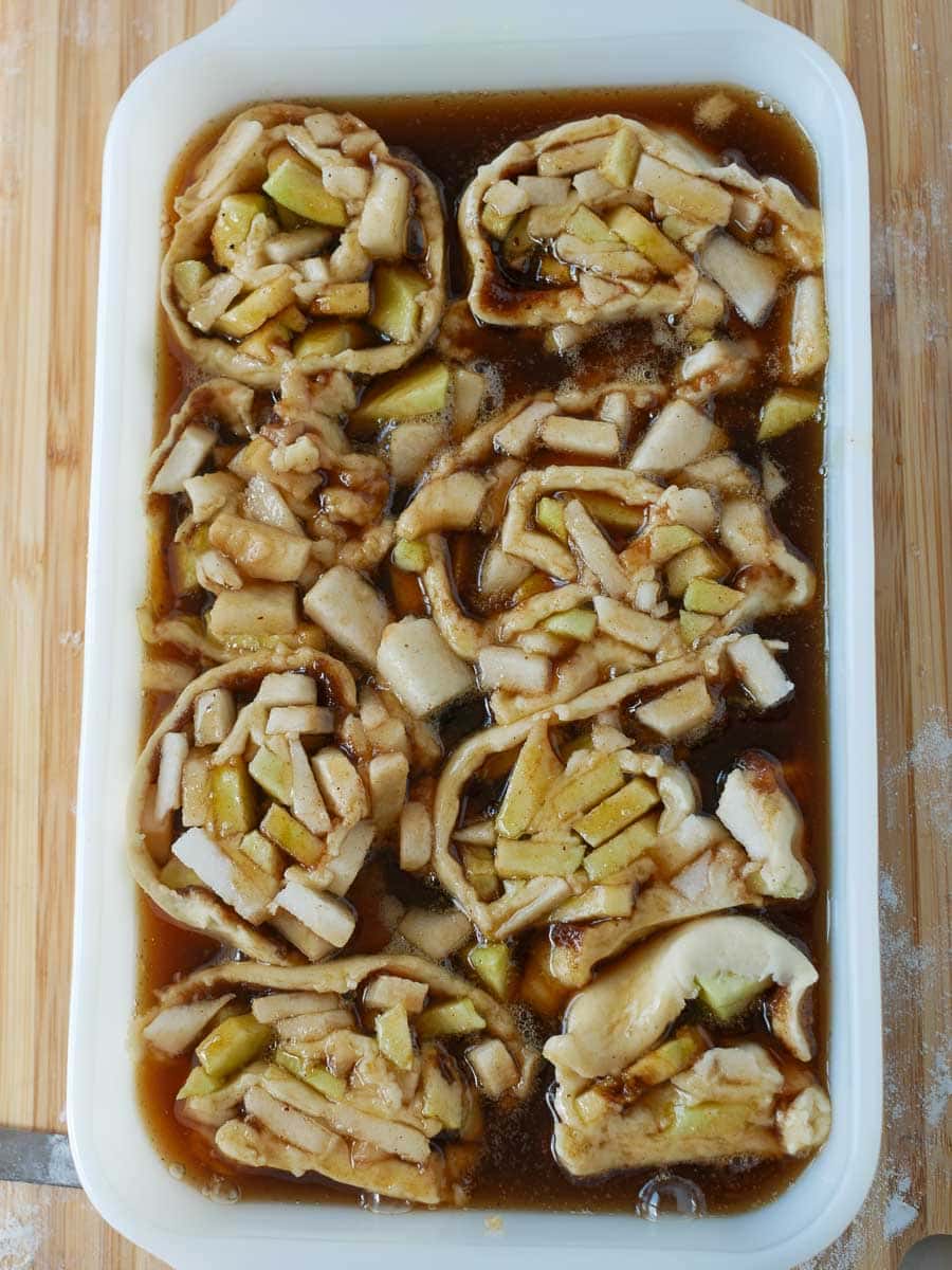 A baking dish filled with sliced apples and pastry dough in a brown syrup, ready for baking.