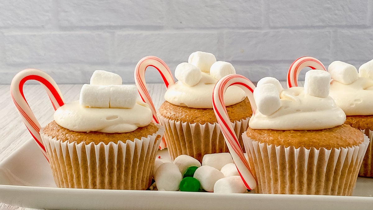 Cupcakes with white frosting, topped with mini marshmallows and candy canes, arranged on a plate.