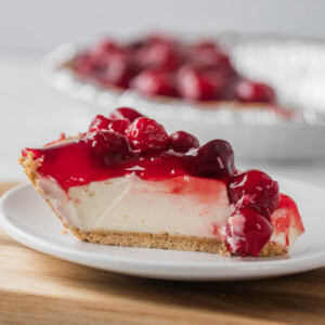 Slice of cherry cheesecake on a white plate, with more cheesecake in the background.