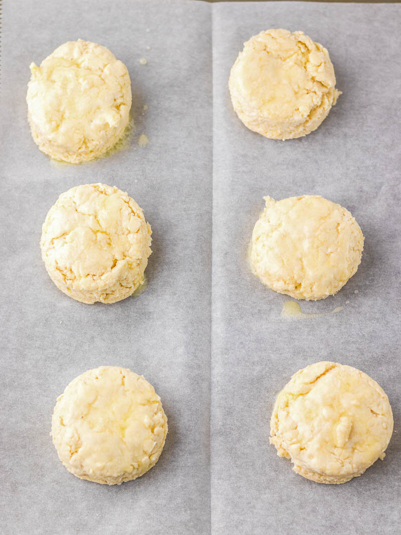 Six unbaked biscuits arranged in two rows on parchment paper.