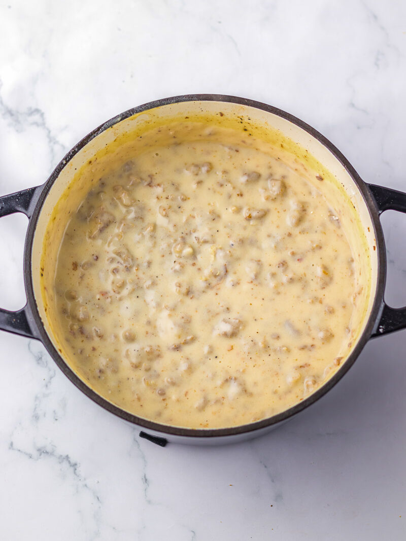 A pot of creamy sausage gravy sits on a white marble surface.