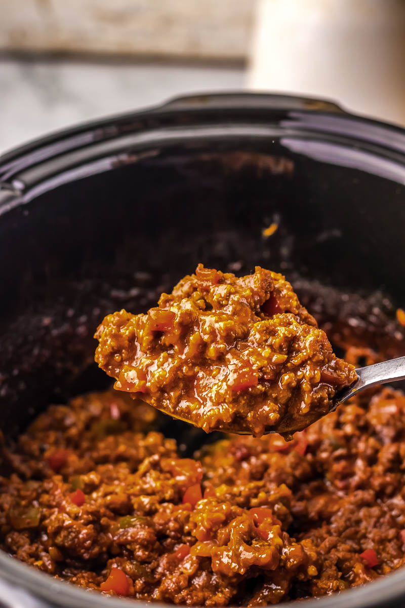 Close-up of cooked ground beef with diced tomatoes being scooped from a black pot.