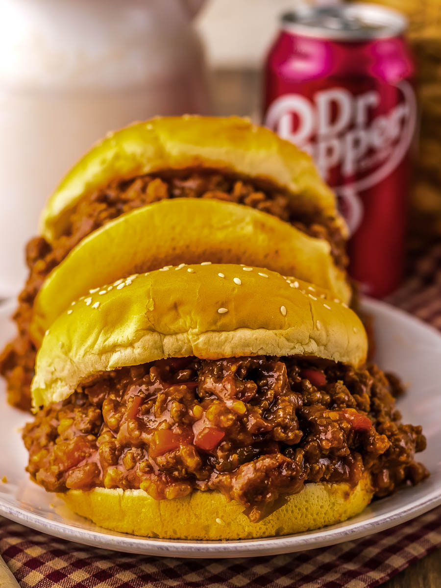 Three sloppy joe sandwiches on a plate with a can of Dr Pepper in the background.
