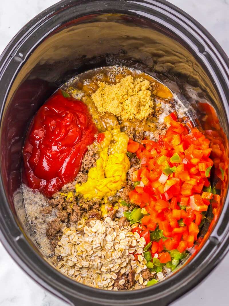 Ingredients in a slow cooker: ground meat, chopped red and green peppers, oats, mustard, ketchup, brown sugar, and sauce, placed separately.