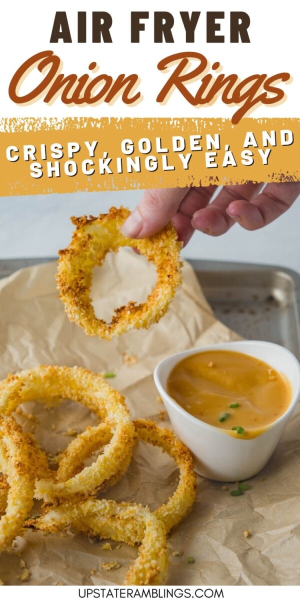 Air fryer onion rings on a baking tray with a hand holding one ring; served with a small bowl of dipping sauce. Text reads: "Crispy, golden, and shockingly easy.