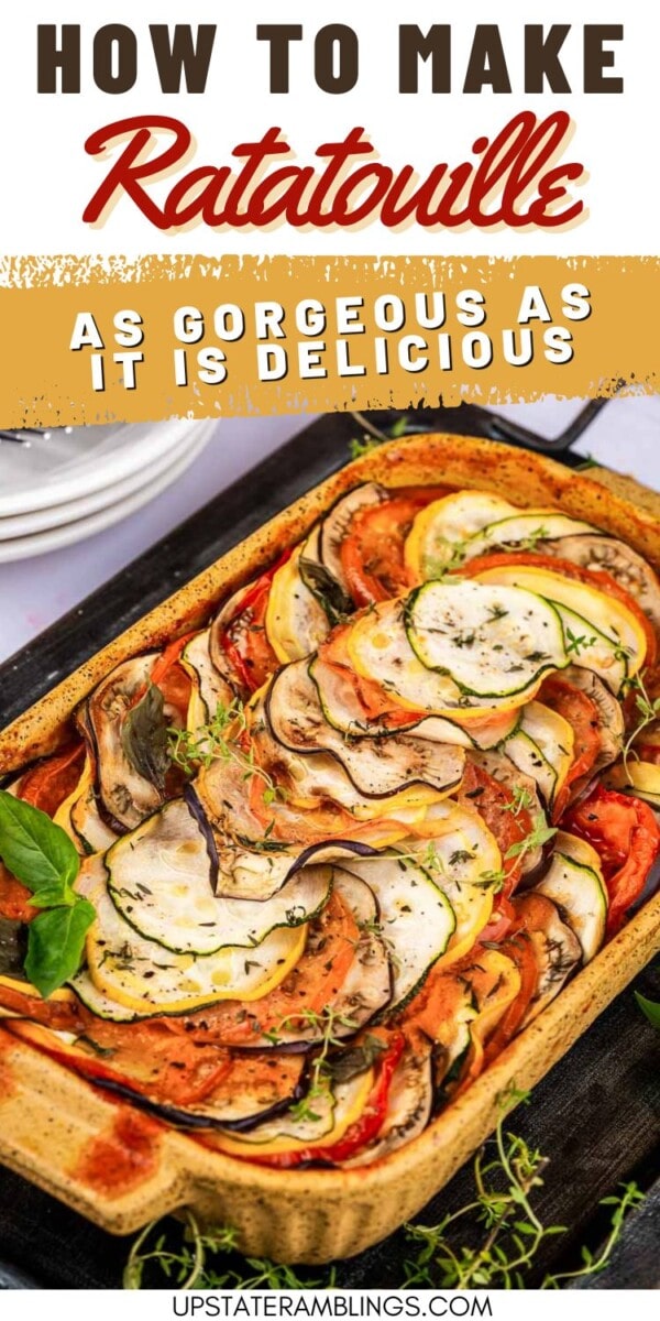 A rectangular baking dish filled with neatly arranged, sliced vegetables for ratatouille, garnished with fresh herbs, sits on a table.