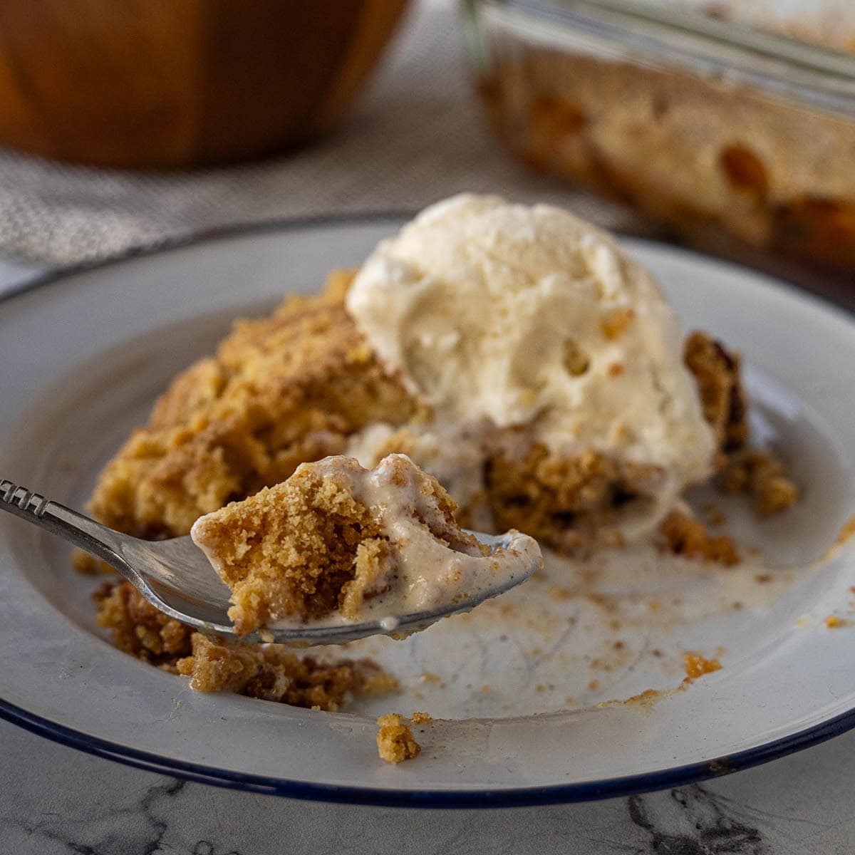 A plate with a serving of crumbly dessert topped with a scoop of vanilla ice cream; a fork holds a bite-sized portion in the foreground.