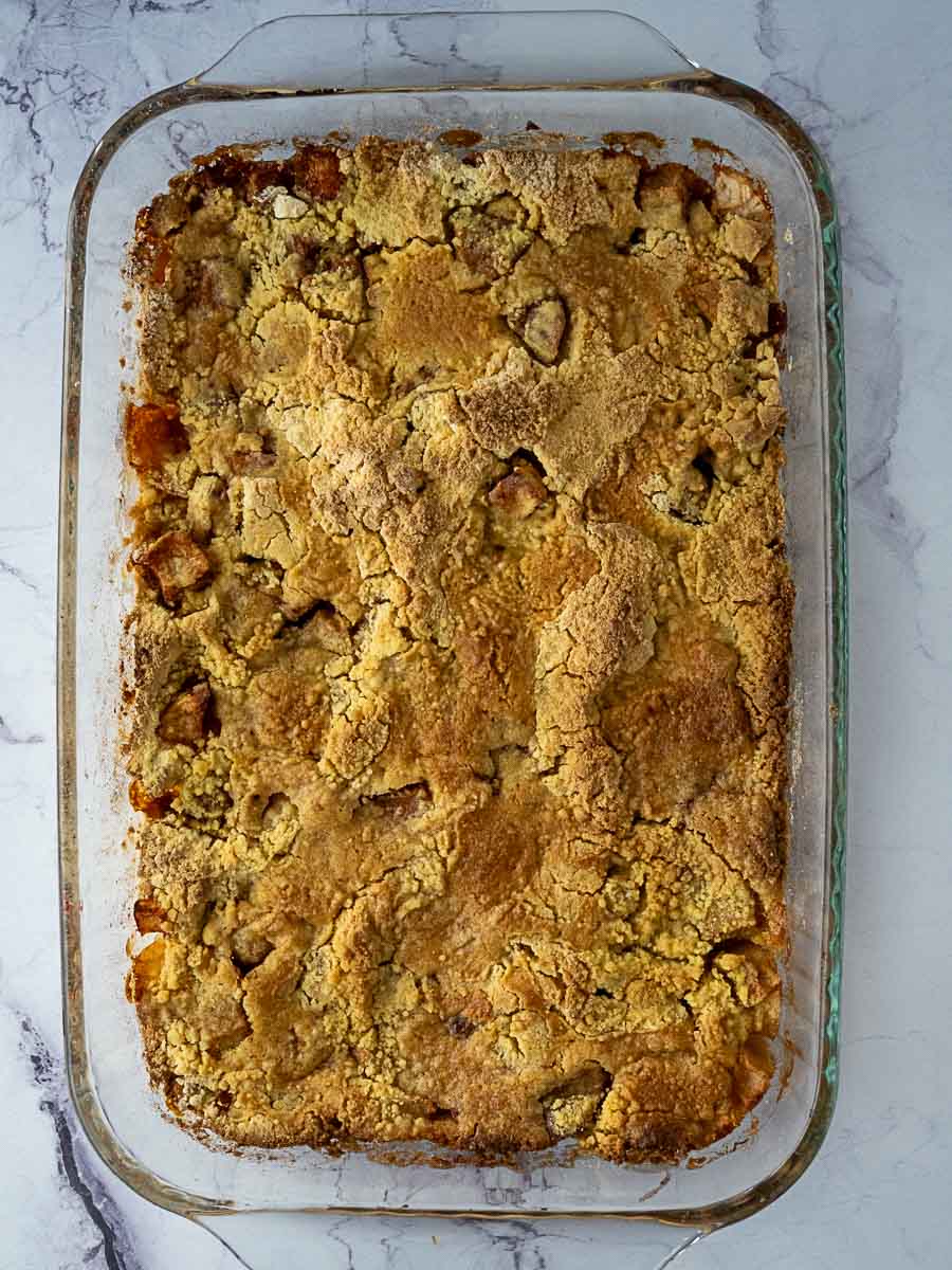 A rectangular glass baking dish filled with a baked dessert featuring a golden-brown, crumbly topping on a marble surface.