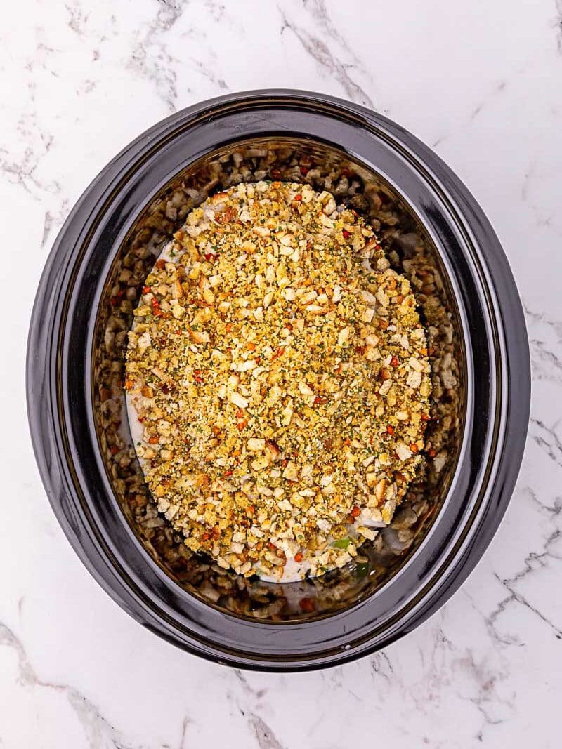An overhead view of a slow cooker containing a breaded and seasoned dish, possibly chicken, on a marble countertop.