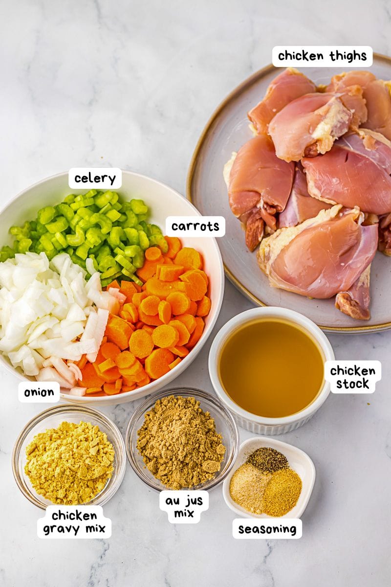 Chopped onion, celery, and carrots with raw chicken thighs, chicken stock, chicken gravy mix, au jus mix, and assorted seasonings displayed on a countertop. Labels identify each ingredient.