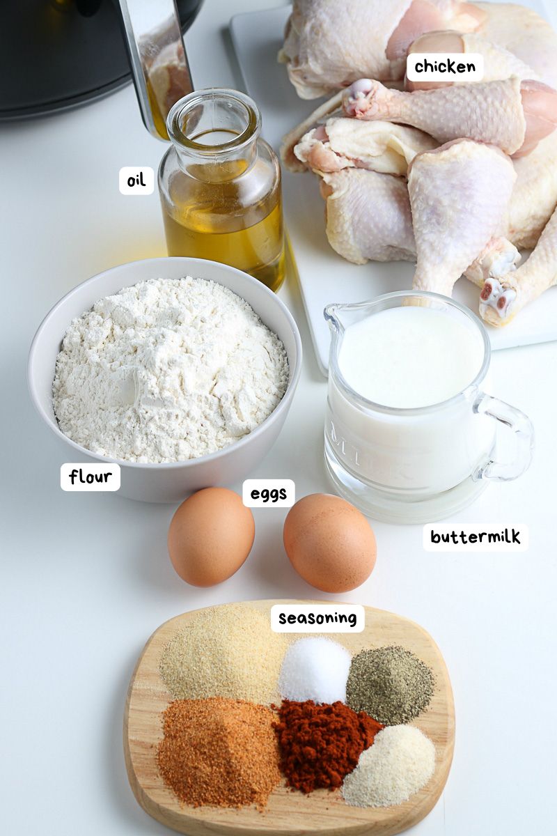 Ingredients for fried chicken: raw chicken pieces, oil, flour, buttermilk, eggs, and various seasonings arranged on a countertop. Labels identify each item.