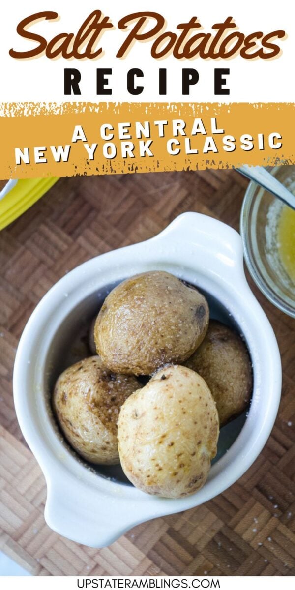 A white bowl filled with cooked salt potatoes sits on a wooden surface, with a glass dish of melted butter partially visible beside it.