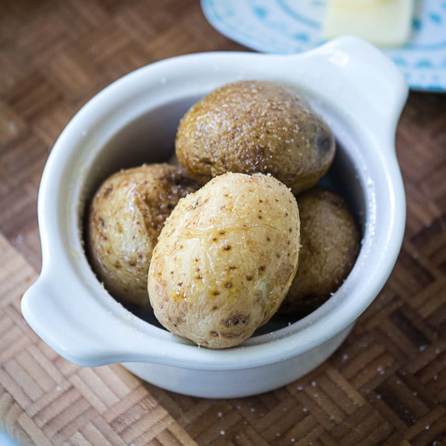 A small white dish contains four roasted baby potatoes with a light sprinkling of salt on their skins.