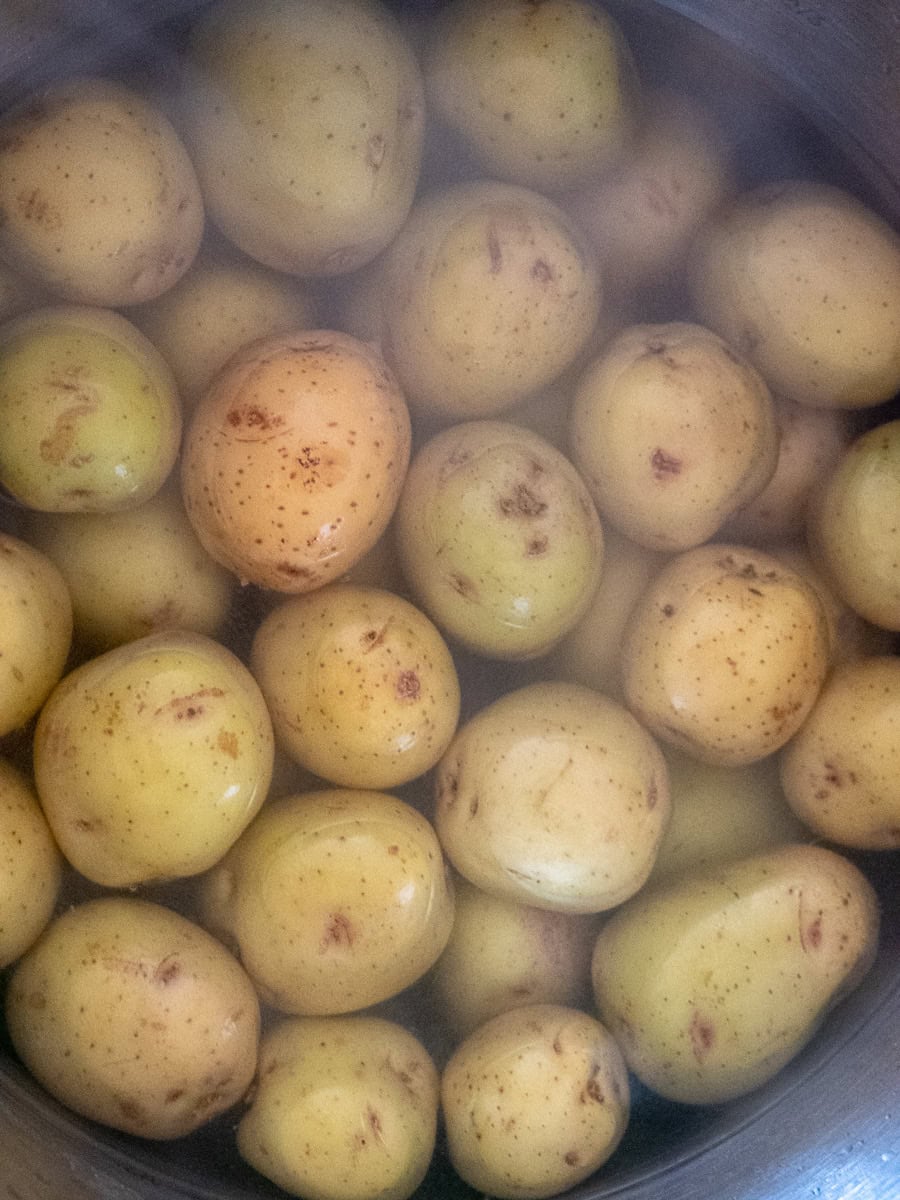 A pot filled with whole, unpeeled potatoes being steamed or boiled, with condensation visible on the surface.