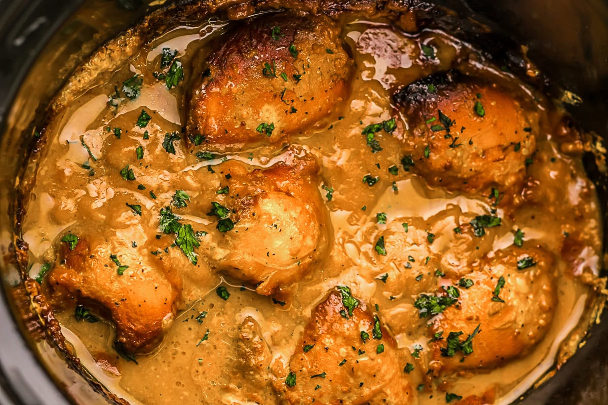 Close-up of cooked chicken thighs in a creamy sauce, garnished with chopped herbs, inside a slow cooker.